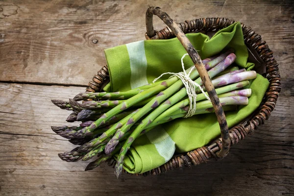 Verse groene asperges in een mand op een rustieke houten tafel, uitzicht van bovenaf — Stockfoto