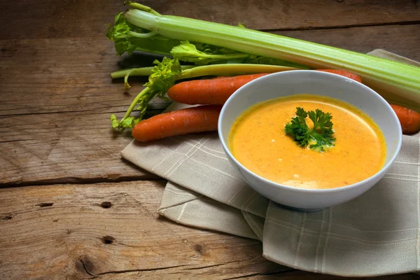 Karottensuppe mit Sahne, Sellerie und Petersilie garniert in einer Schüssel auf rustikalem Holz, Kopierraum — Stockfoto