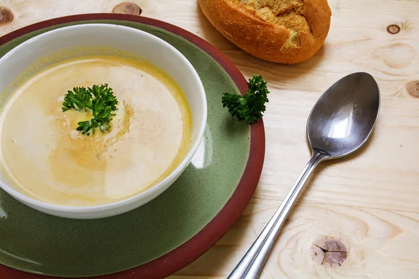 Sopa de crema con guarnición de perejil en un tazón en un plato verde, pan y cuchara en una mesa de madera — Foto de Stock