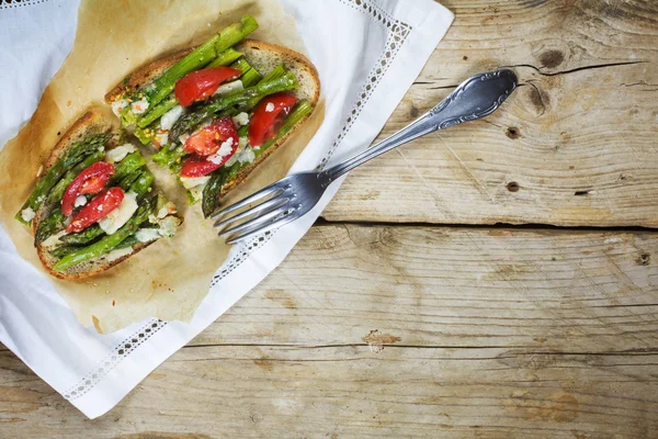 Green asparagus, tomatoes and parmesan gratinated on roasted bread from above, copy space — Stock Photo, Image