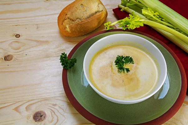 Gemüsecremesuppe mit Sellerie und Petersilie garniert in einer Schüssel auf einem grünen Teller, Holzgrund — Stockfoto