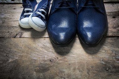 father's shoes and kids sneakers side by side on rustic wood  clipart
