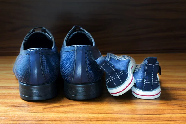 Men shoes and children sneakers side by side on the wooden floor, father's day — Stock Photo, Image