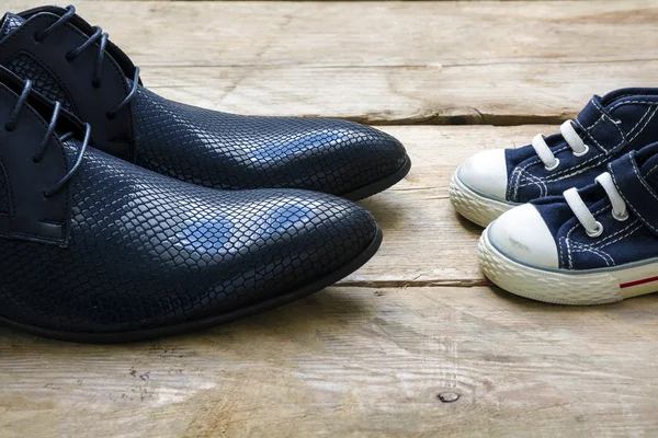 Mannen schoenen en kids sneakers staan tegenover elkaar op een hout, vader's dag — Stockfoto