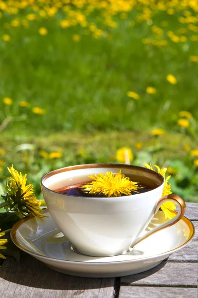 Dandelion tea in a white cup on a wooden table against a blurred maedow, vertical — Stock Photo, Image