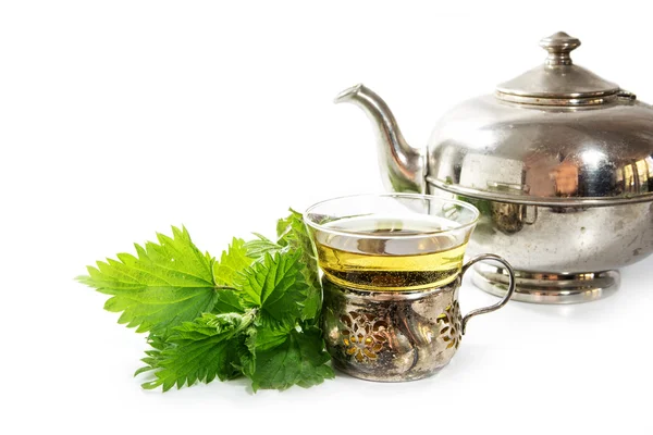 Серебряный чайник и винтажный стакан с крапивой чай и некоторые свежие листья, белый фон — стоковое фото
