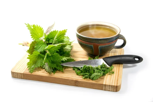 Voorbereiding van de brandnetel thee, verse bladeren, mes en een rustieke theekopje op een houten snijplank, geïsoleerd — Stockfoto