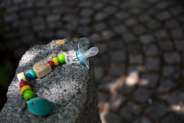 Chupete de bebé con una cadena hecha de elementos de madera dejados en una piedra de granito —  Fotos de Stock