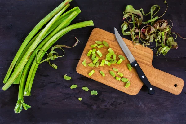 Rhubarb stalks and spirals from the peel, sliced pieces and a wooden kitchen board, dark background, view from above — Stock Photo, Image