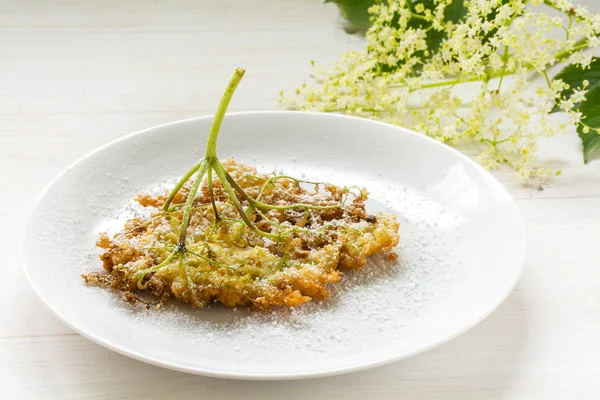 Fleur de sureau frite en pâte à crêpes avec sucre en poudre sur une assiette sur une table en bois blanc — Photo