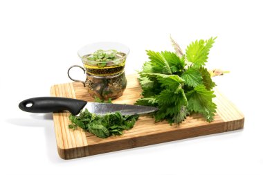 Beyaz yaprakları ve ısırgan otu çayı ile bir fincan dilimlenmiş bir kesme tahtası üzerinde ısırgan, bıçak, demet izole