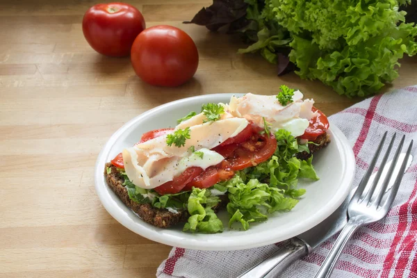 Pan de centeno integral con tomates, ensalada verde y filete de pechuga de pollo en una tabla de cocina de madera — Foto de Stock