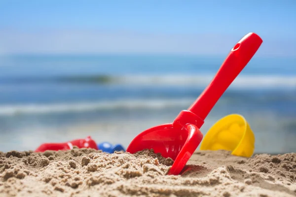 Pala de juguete rojo y moldes de plástico en la arena en la playa, mar borroso n el fondo —  Fotos de Stock