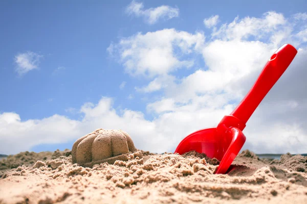 Rote Spielzeugschaufel und geformter Sand am Strand gegen den blauen Himmel — Stockfoto