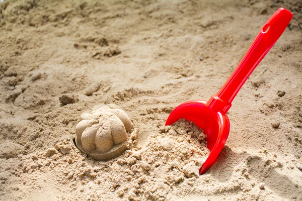 red toy bucket and molded sand in a sandbox or at the beach