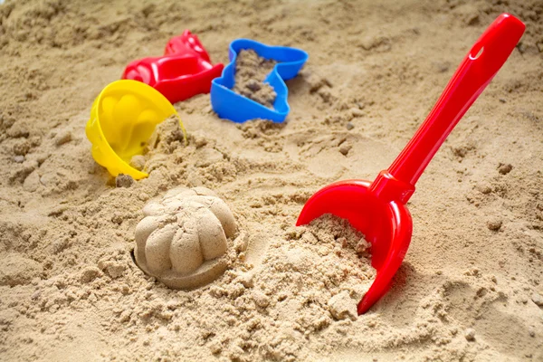 Kırmızı oyuncak kürek ve renkli plastik kalıpları bir kum veya sahilde — Stok fotoğraf