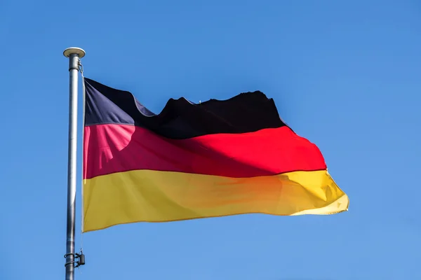 Bandera alemana ondeando en el viento contra el cielo azul claro — Foto de Stock