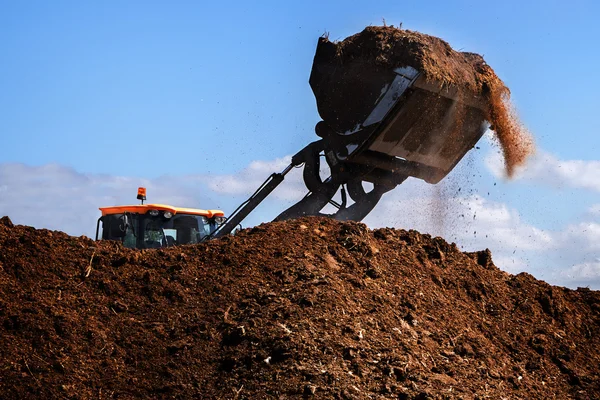Pá escavadora trabalhando em um grande monte de estrume, fertilizante orgânico — Fotografia de Stock