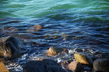 Deniz kıyısında turkuaz mavi okyanusun nazik sörf içinde taş olan
