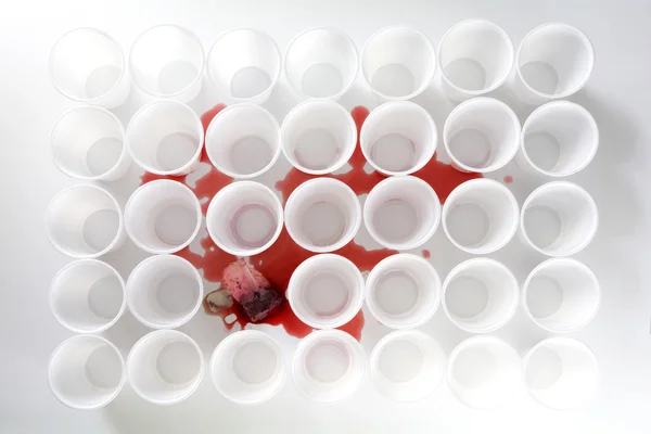 Bleeding teabag with red tea between rows of white plastic cups, mobbig victim — Stock Photo, Image