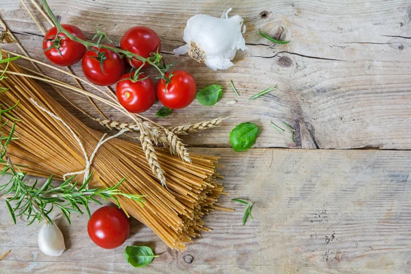 Ingrédients pour un repas de pâtes italiennes avec spaghettis complets, tomates, ail et herbes, vus d'en haut sur du bois rustique — Photo