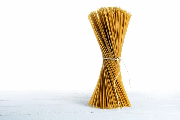 Bunch of standing wholemeal spaghetti on white wood against a white background, copy space — Stock Photo, Image