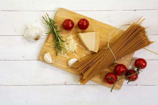 Kitchen board med ingredienser för en italiensk måltid sett från ovan med fullkorn spagetti, tomat, parmesan och örter — Stockfoto