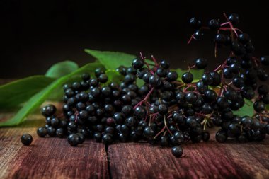 Eski bir kil kase bir rustik ahşap masa karanlık bir arka plan üzerinde siyah elderberries grup (Sambucus nigra)