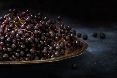 Rustik ahşap bir masa karanlık bir arka plan üzerinde eski bir gümüş tepside siyah elderberries grup (Sambucus nigra)