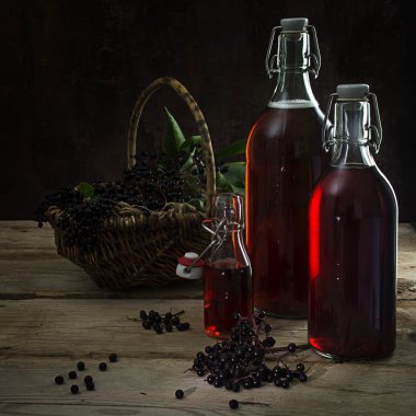 siyah elderberries (Sambucus nigra) ve bir sepet ile çilek rustik ahşap, koyu arka plan üzerinde kırmızı suyu şişeleri