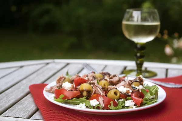 Tonfisk sallad med tomater, oliver och ruccola, serveras med vin i trädgården på ett träbord — Stockfoto