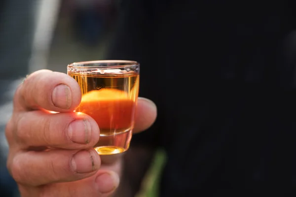 Brudny mężczyźni ręka trzyma kieliszek z napój pomarańczowy alkoholu, tło robi się czarny — Zdjęcie stockowe
