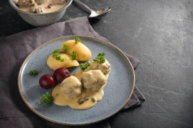 Boiled meatballs in Germany called Koenigsberger Klopse in a white bechamel sauce with capers, potatoes and beetroot on a blue plate, dark gray napkin and slate background with copy space, selected focus, narrow depth of field clipart