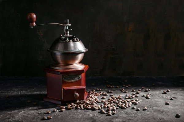 Nostalgic wooden coffee grinder and roasted coffee beans in side light against a dark rustic background with copy space, selected focus