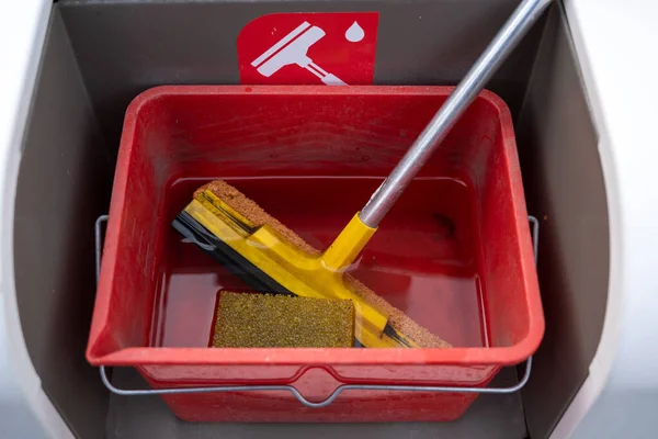 Cleaning set with squeegee, sponge and water for car windscreens in a red bucket at a gas station , selected focus, narrow depth of field