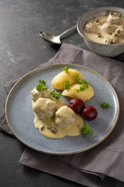 Koenigsberger Klopse ya da kapari, patates ve pancar soslu beyaz bechamel soslu haşlanmış köfteler, peçete ve fotokopi alanı ile koyu gri arka plan, seçilmiş odak, dar alan derinliği