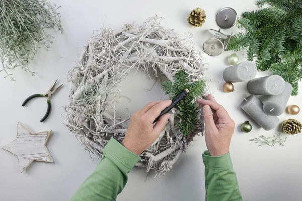 緑のモミの枝 灰色のろうそく 白いテーブルの上からの高い角度のビューでクリスマスの装飾と淡い木材からの出現花輪を作る女性の手 — ストック写真