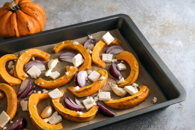 Çiğ balkabağı dilimleri, kırmızı soğanlar ve fırın için feta peyniri ile pişirme tepsisi, Şükran Günü ve Cadılar Bayramı 'nda sonbahar sebzeleriyle pişirme, seçilmiş odak, dar tarla derinliği