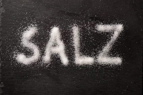 德语单词Salz 意为盐 用黑色石板上的盐晶体书写 从上方高角度观看 选择焦点 — 图库照片