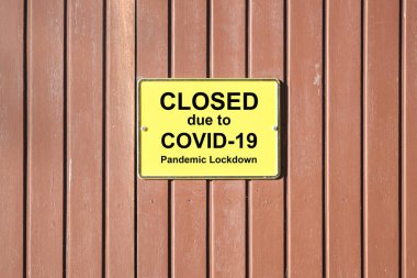 Panjurlu ahşap kapı, sarı bir işaret ve metin. Covid-19 Pandemik Kilitlenme nedeniyle kapatıldı. Birçok perakendeciler Coronavirus krizi sırasında bunu yapmak zorunda kaldı.