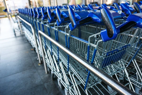 Blue handles of shopping carts in a row waiting for customers in front of a retail store during lockdown due to covid-19 pandemic, copy space, selected focus