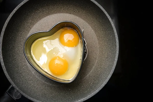 黒いストーブの上のフライパンにハート型の2つの目玉焼き ロマンチックなバレンタインデーの朝食の準備 コピースペース 上からの高い天使の眺め — ストック写真