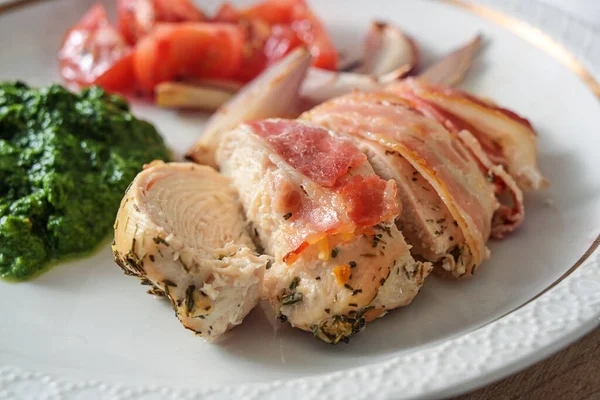 Hühnerbrustfilet Speckmantel Mit Spinatpüree Zwiebeln Und Tomaten Auf Einem Teller — Stockfoto