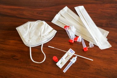 Covid-19 hızlı antijen test kiti negatif sonuç, burun çubukları, tüpler, tespit cihazı ve kahverengi ahşap bir masa üzerinde cerrahi ffp-2 yüz maskesi, kopyalama alanı, yukarıdan yüksek açı görünümü