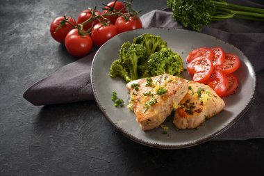 Brokoli ve domatesli kızarmış ton balığı filetosu, gri tabakta maydanoz ve limon aromalı garnitür ve siyah tahta masa, kopyalama alanı, seçilmiş odak ve dar alan derinliği