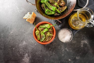 Koyu gri bir arka planda kızarmış biber veya tavada yeşil biber ve geleneksel İspanyol tapa kasesi, tuz, zeytin yağı ve ekmek, kopyalama alanı, yukarıdan yüksek açı, seçilmiş odak noktası.