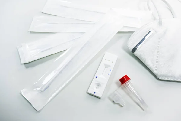 Rapid antigen self test kit for Covid-19 diagnostic at home with nasal swabs, tubes, detection device and a ffp-2 face mask, light gray background, copy space, high angle view from above, selected focus