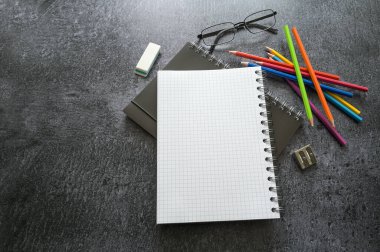 Yaratıcı ofis masası, sarmal defterler, renkli kalemler, koyu gri bir masa üzerindeki gözlükler ve malzemeler, kopyalama alanı, seçilmiş odak, dar alan derinliği