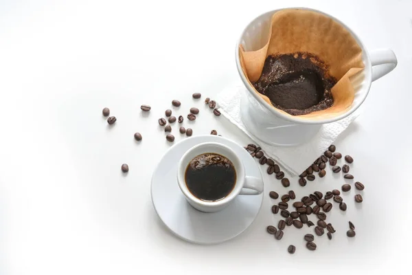 Coffee in a cup and ground coffee in a filter bag, drip brewed hot drink, light background fading to white with some beans, copy space, selected focus, narrow depth of field