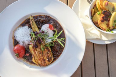 Patatesli et yahnisi, domates, kavrulmuş rezene ve garnitürlü tereyağı, süs köpüğü ile servis edilen beyaz tabakta ve kızarmış patatesli bir kase, yukarıdan yüksek açılı görüş, seçilmiş odak noktası.